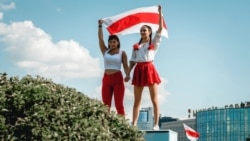 Two women display a former Belarusian national flag, a symbol of opposition to the government, during a Minsk rally on August 16, 2020 against police violence and Belarus' official presidential election results.