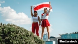 Two women display a former Belarusian national flag, a symbol of opposition to the government, during a Minsk rally on August 16, 2020 against police violence and Belarus' official presidential election results.